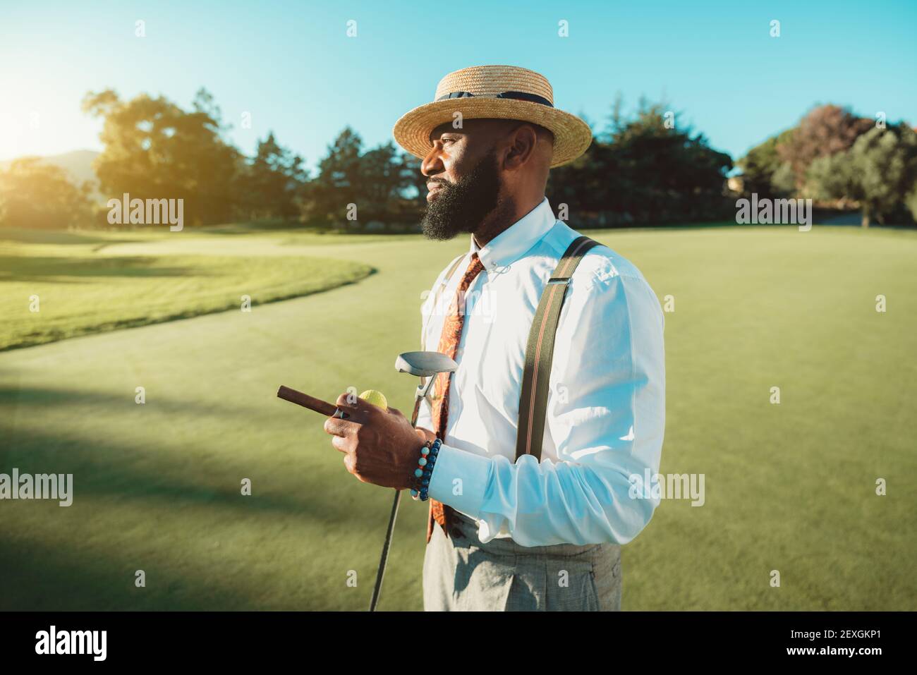 Un ritratto di un bel dapper uomo nero con il portamento in un abito  elegante: Camicia bianca, pantaloni con sospenditori, cravatta, e cappello,  è in piedi sul golf f Foto stock -
