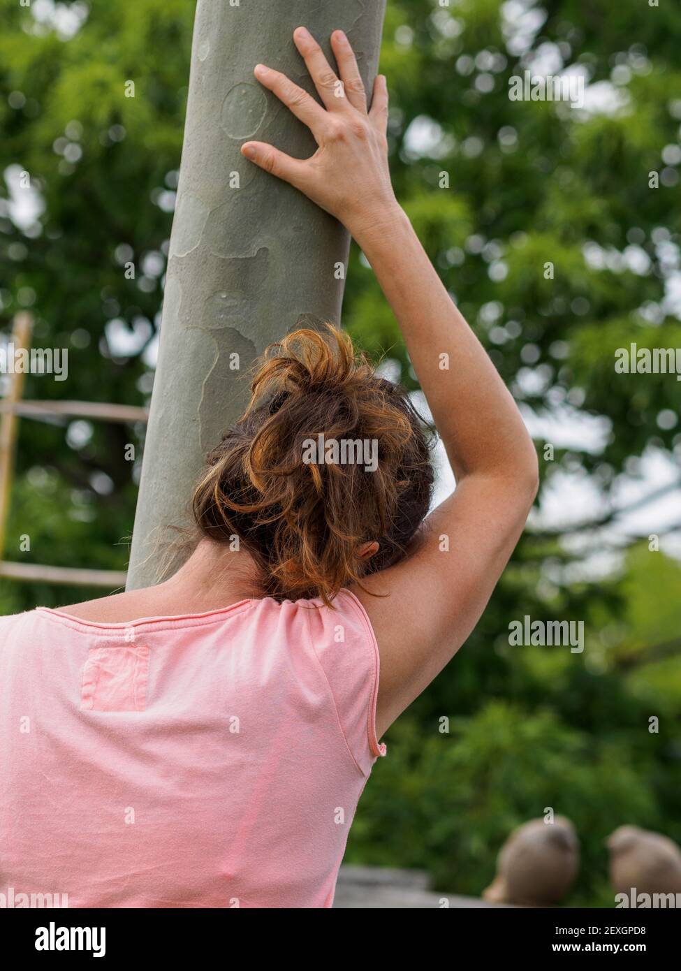 Giovane donna caucasica stanca si appoggia al tronco d'albero nel parco estivo. Tempo per rilassarsi. Concetto di salute mentale. Da dietro. Foto Stock