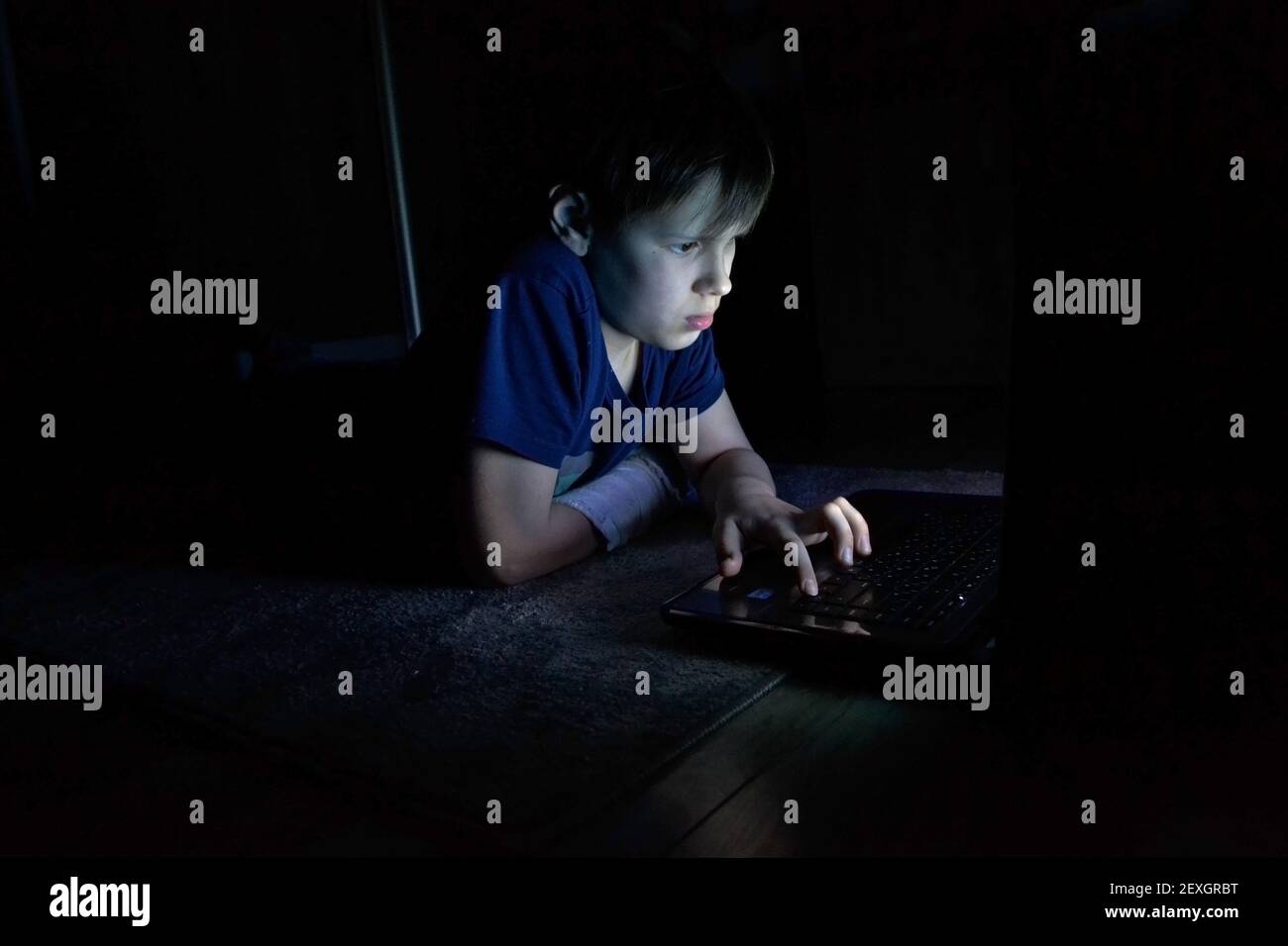 ritratto del ragazzo che usa un computer portatile in una stanza buia Foto Stock
