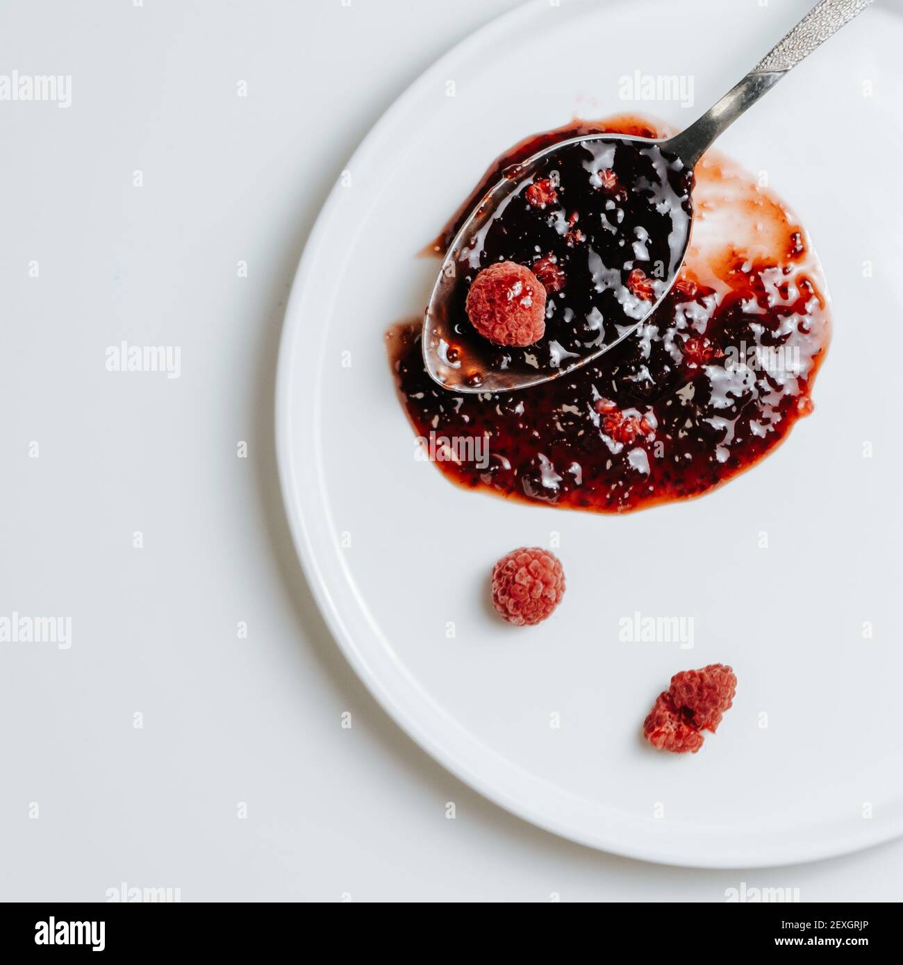 Cucchiaio di confettura di lamponi su un piatto bianco con surgelato bacche Foto Stock