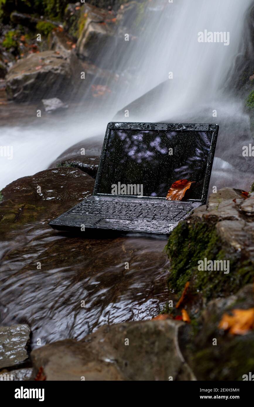 Telelavoro Concept.Waterproof centro di servizio omputer. Computer portatile bagnato con sfondo a cascata slow motion. Acqua corrente. Foto Stock