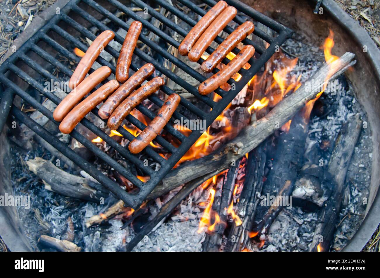 Arrostire il hot dog su un falò a fiamma libera. Grigliare deliziosi carne hot dog sopra la fossa del fuoco. Campeggio e cucina pic-nic pranzo o cena all'aperto. Foto Stock