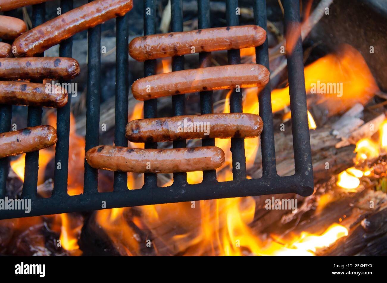 Arrostire il hot dog su un falò a fiamma libera. Grigliare deliziosi carne hot dog sopra la fossa del fuoco. Campeggio e cucina pic-nic pranzo o cena all'aperto. Foto Stock
