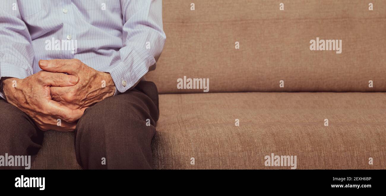 Un vecchio caucasico irriconoscibile seduto sul divano in soggiorno. Concentrarsi sulle mani. Spazio di copia. Solitudine totale in età avanzata. Banner. Foto Stock