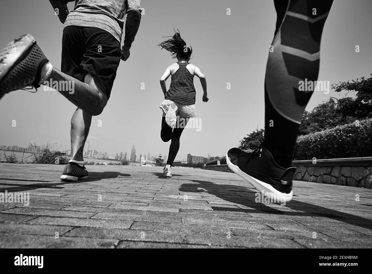 tre giovani adulti asiatici che corrono all'aperto, vista posteriore e ad angolo basso, in bianco e nero Foto Stock