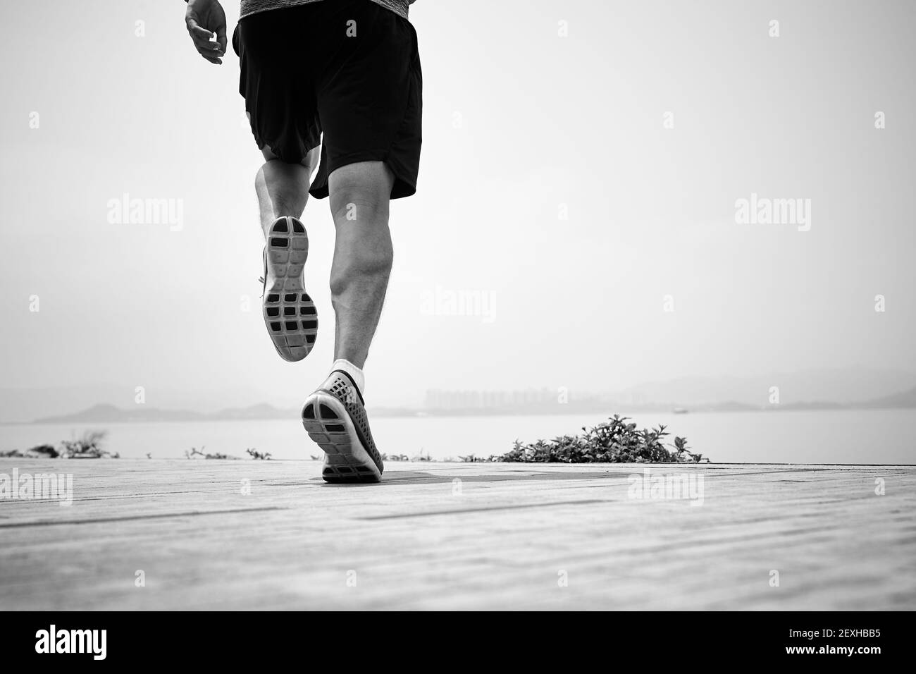 primo piano delle gambe di un corridore asiatico che corre sul mare, vista posteriore, in bianco e nero Foto Stock