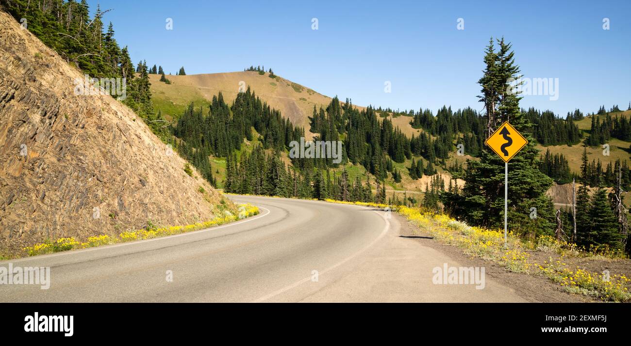 Il segnale stradale indica le curve che precedono il paesaggio montano Foto Stock