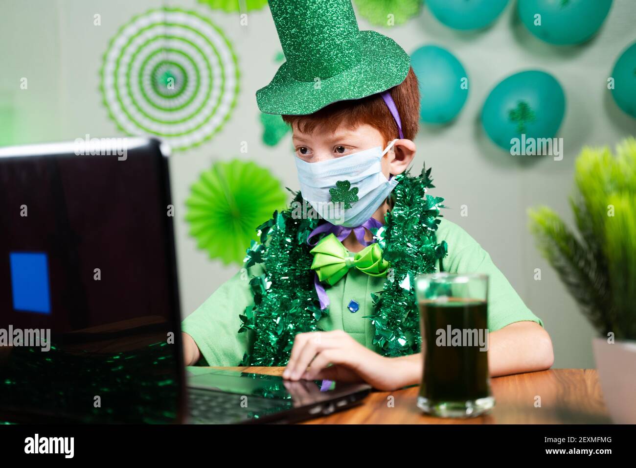 Bambino giovane con maschera facciale occupato in videochiamata su Laptop su sfondo decorato - concetto di San Patrizio lontano festa di giorno a causa del coronavirus Foto Stock