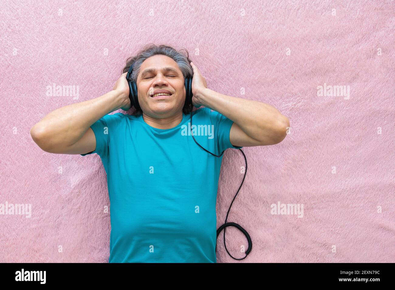 l'uomo di 50 anni ascolta la musica con le cuffie a casa, sdraiato sul letto. Relax, piacere. Foto Stock