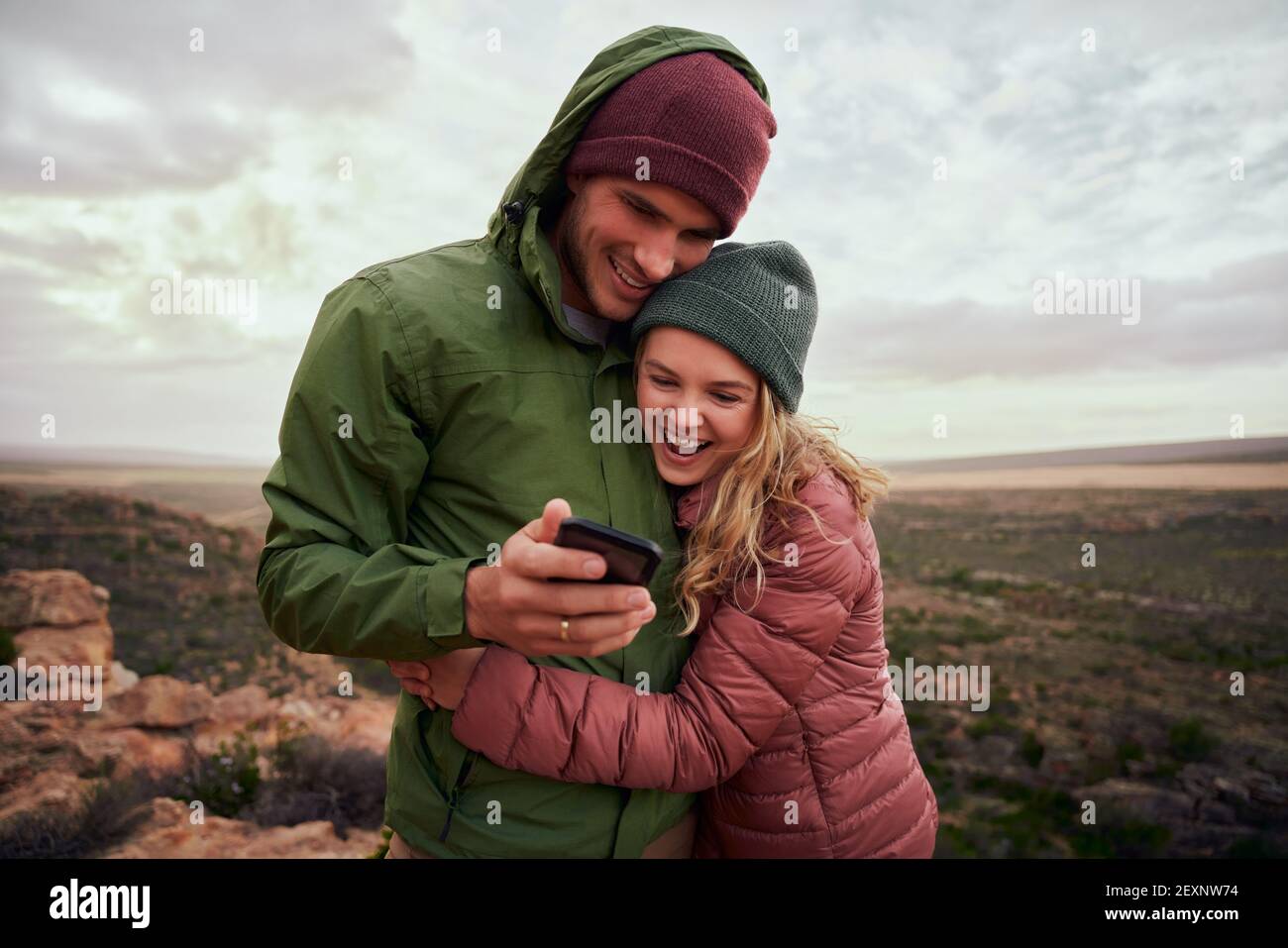 Ridendo giovane coppia abbracciando durante il campo sulle montagne guardando smartphone con abbigliamento invernale Foto Stock