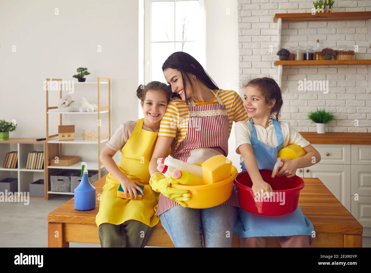 Madre sorridente e due figlie sedute a tavola con la famiglia per la pulizia della casa Foto Stock