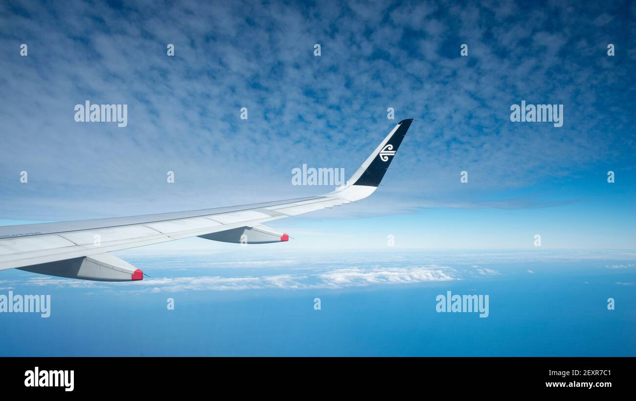 Vista aerea di un'ala di aeroplano con il logo Air New Zealand su di essa. Cielo blu con soffici nuvole bianche nel cielo e mare blu sotto. Immagine acquisita Foto Stock