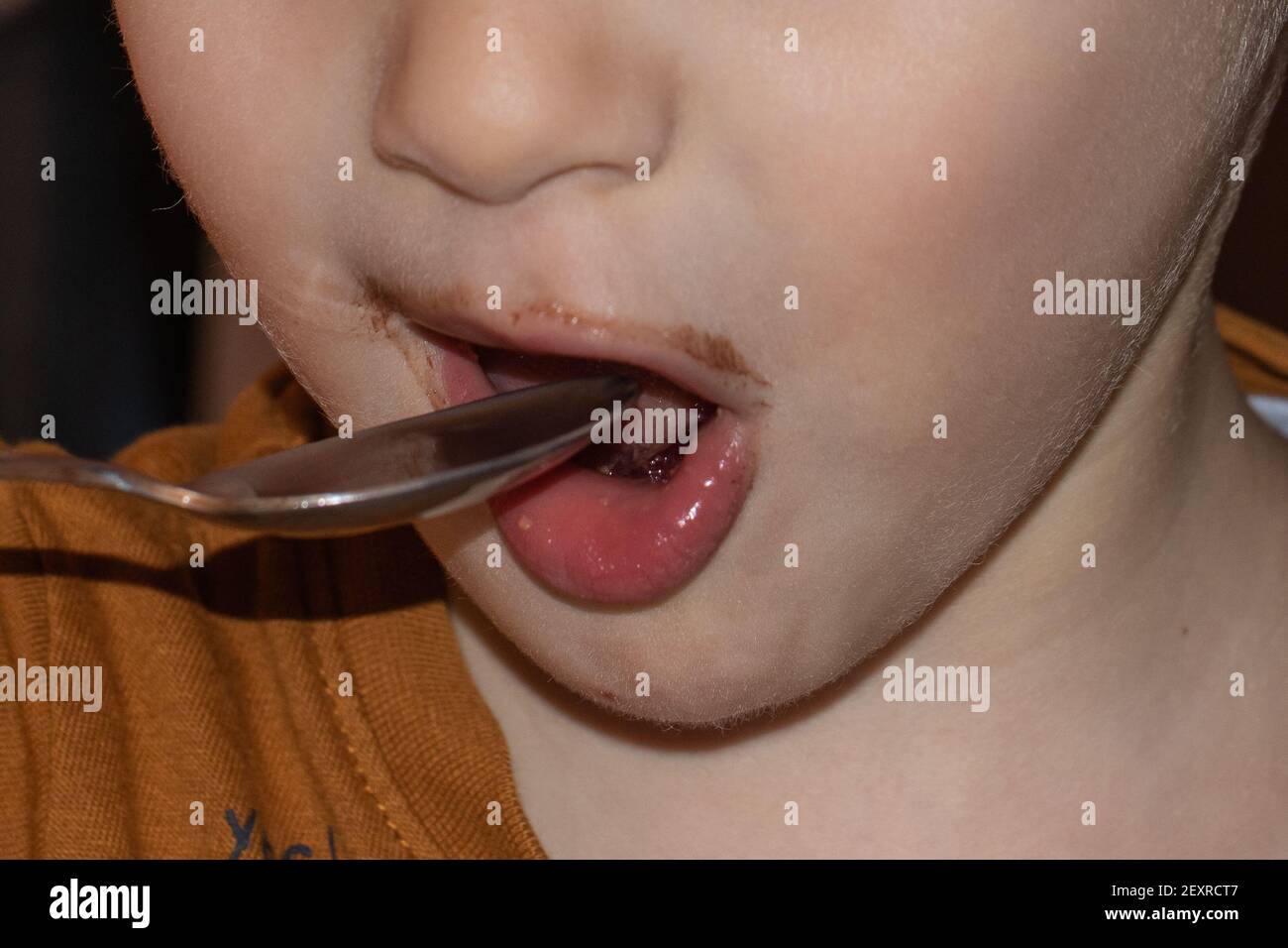 primo piano della bocca di un bambino con le labbra macchiate di cioccolato che è portando un cucchiaio in bocca Foto Stock