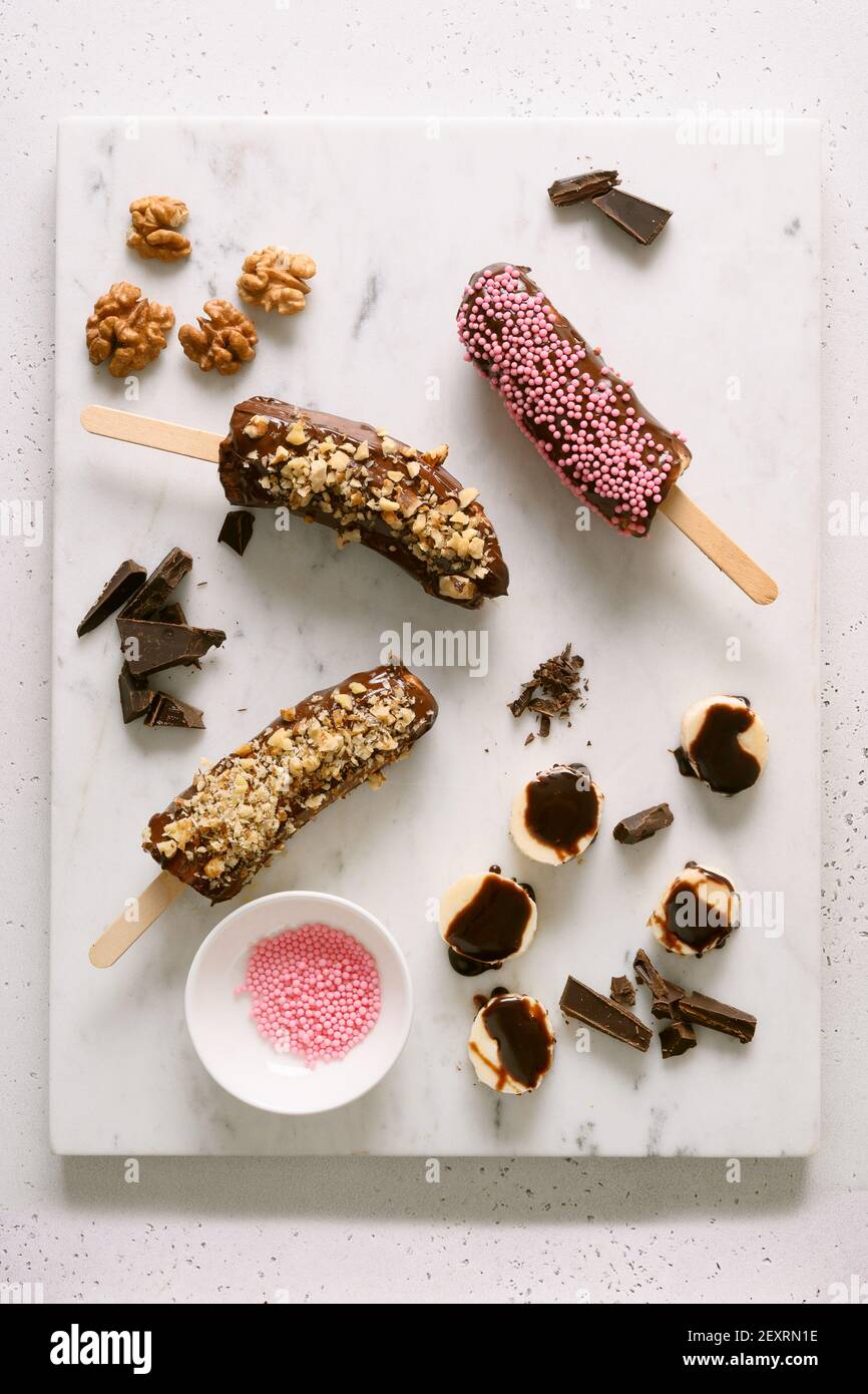 Banane surgelate e lecci di cioccolato con noci e spruzzi rosa. Dolci vegani fatti in casa. Vista dall'alto. Foto Stock