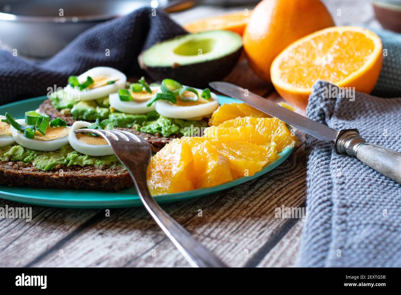 Sandwich aperto con avocado e uova bollite a fette servite con frutta fresca su un piatto di bambù su tavolo da cucina a. casa Foto Stock