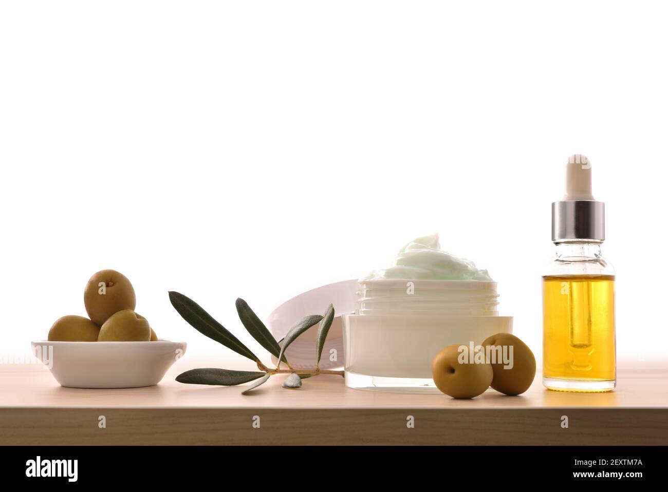 Crema cosmetica al siero e idratante con estratto di oliva per la pelle con rametto e olive su tavola di legno. Vista frontale. Foto Stock