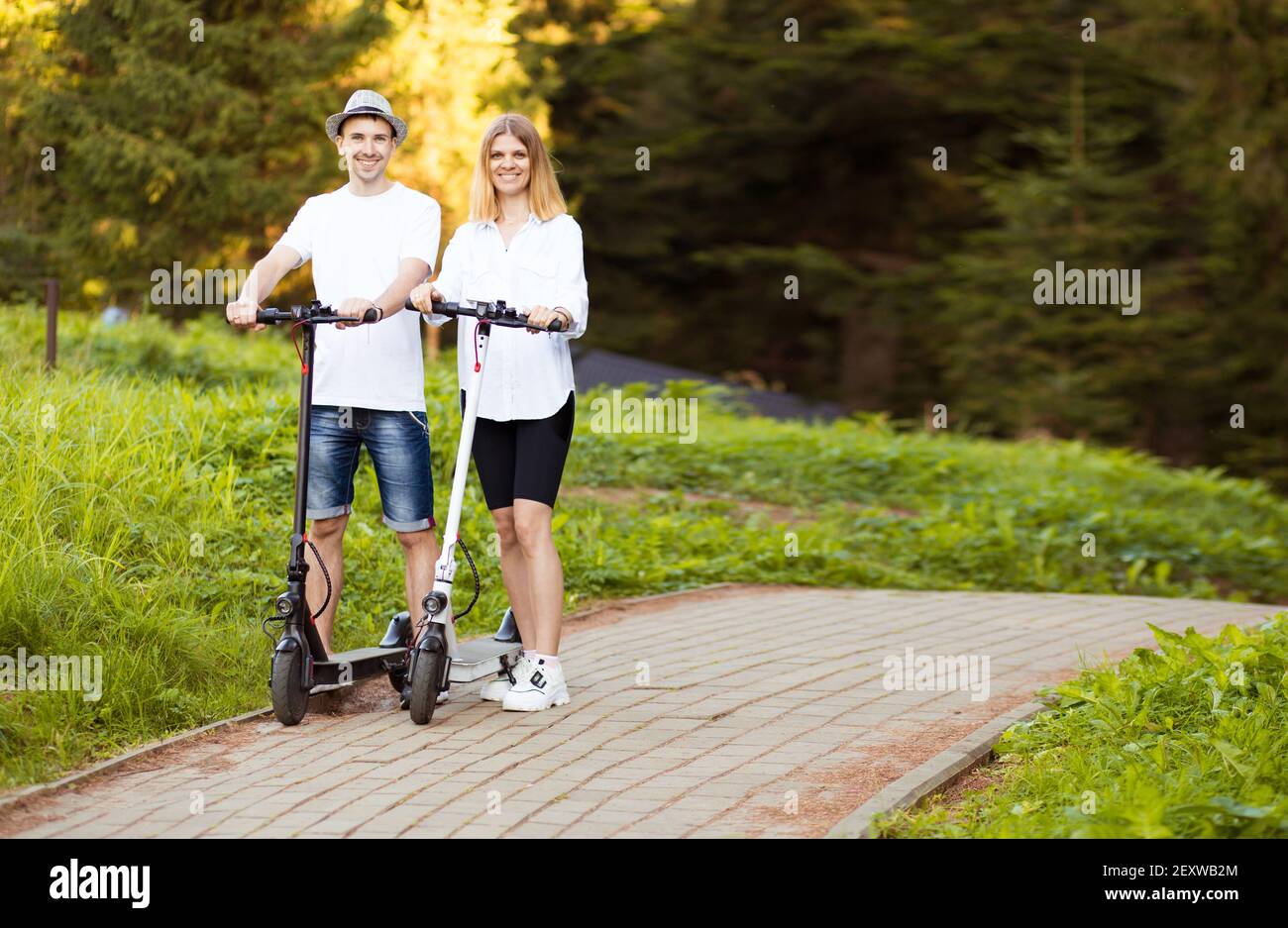 Felice coppia moderna di uomo e donna godendo eco ride in scooter elettrico in giornata di sole in vacanza. Divertirsi insieme guidando uno scooter elettrico attraverso il centro della città. Foto Stock