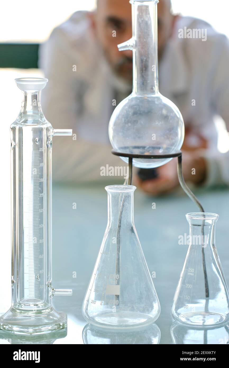 Scienziato maschile che cerca di indossare un camice da laboratorio con fiasche di vetro in un laboratorio scientifico. Paesi Baschi, Spagna, Europa. Foto Stock