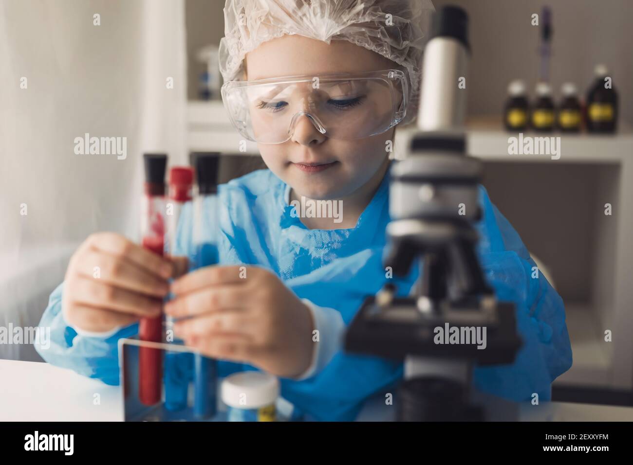 Bambina in laboratorio cappotto di apprendimento chimica in laboratorio  scolastico. Giovane scienziato in occhiali protettivi che fanno esperimenti  in laboratorio o in armadi chimici. Guardando attraverso il microscopio.  Foto di alta qualità