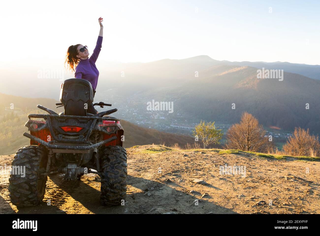 Felice attivo pilota femminile godendo di guida estrema su quad ATV moto in autunno montagne al tramonto. Foto Stock