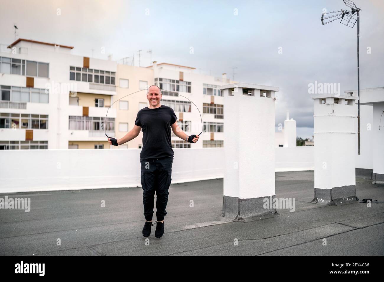 Un uomo che si esercita sul tetto utilizzando una corda che salta durante il blocco, Portogallo Foto Stock