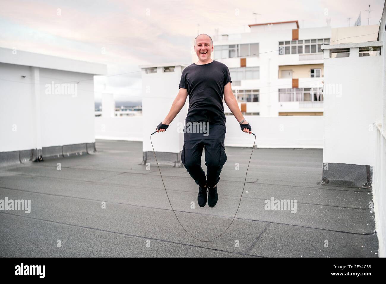 Un uomo che si esercita sul tetto utilizzando una corda che salta durante il blocco, Portogallo Foto Stock
