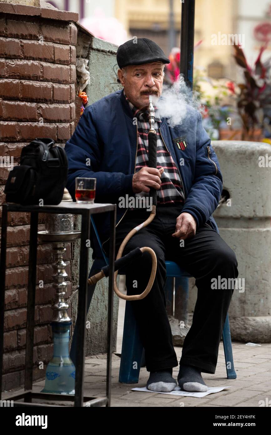 Ritratto di un uomo egiziano locale seduto in un bar a bordo strada (ahwa) che fuma un narghilè, nel centro del Cairo, Egitto Foto Stock
