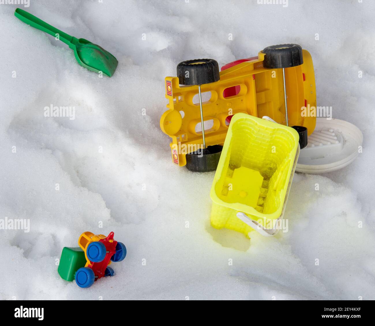 Giocattoli dimenticati per bambini scoop verde, macchina da scrivere, secchio giallo, grande auto gialla nella neve. Primo piano. Senza persone. Foto Stock