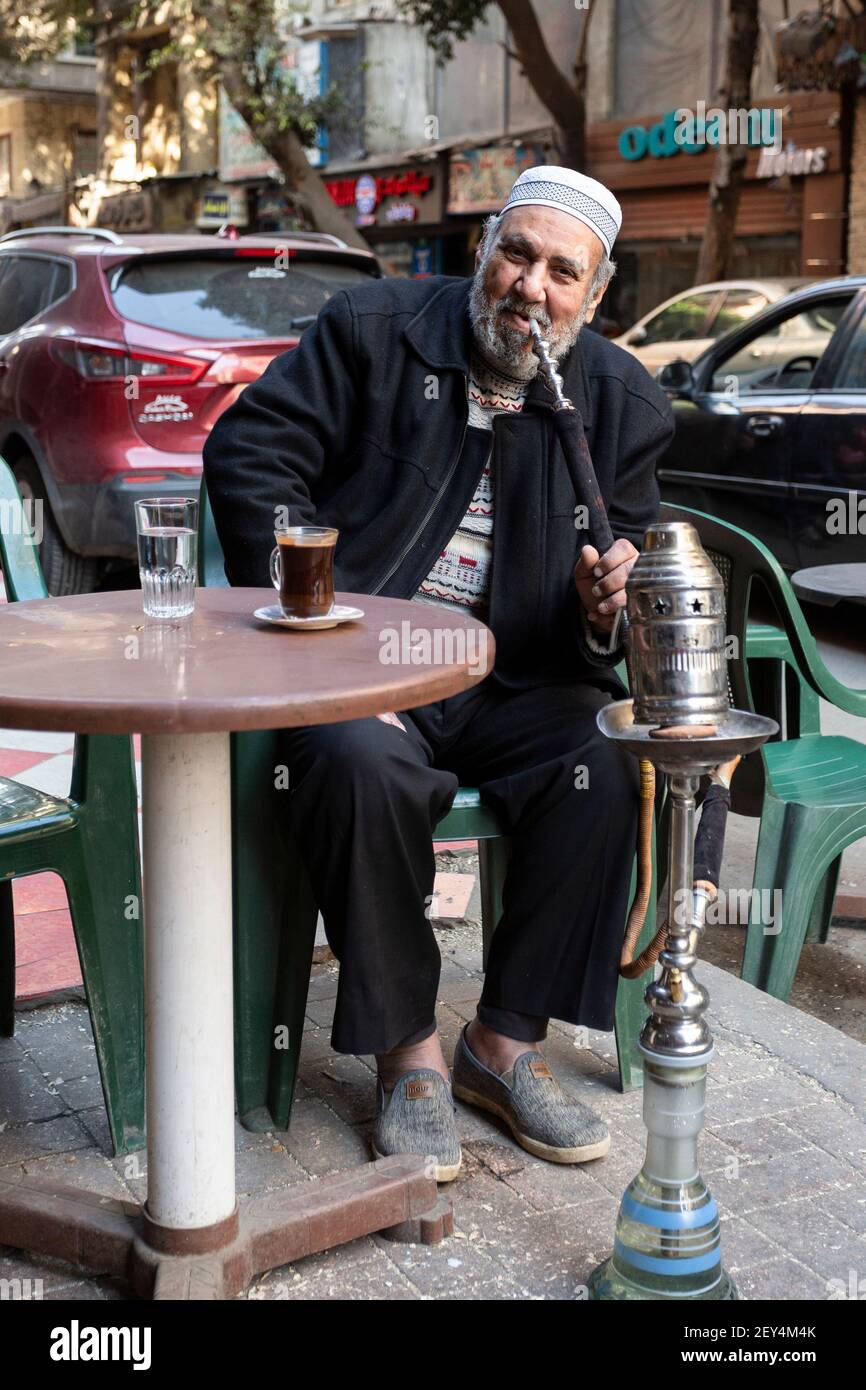 Ritratto di un uomo egiziano locale che fuma una pipa di narghilè in un bar sulla strada (ahwa) nel centro di Cairo, Egitto Foto Stock