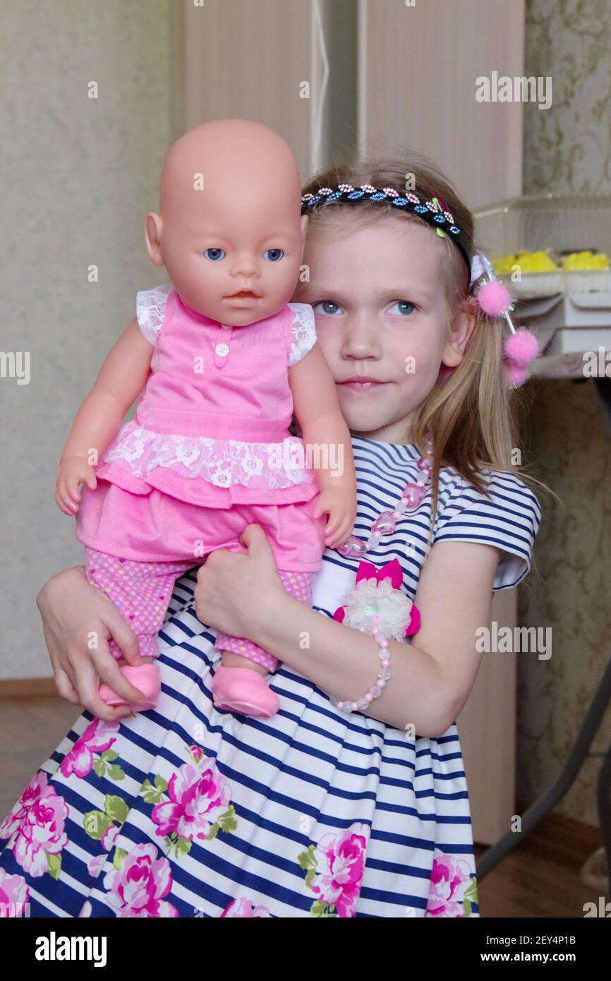 ragazza bionda caucasica con acconciatura in un abito a righe gioca con una bambola in abiti rosa. Foto Stock