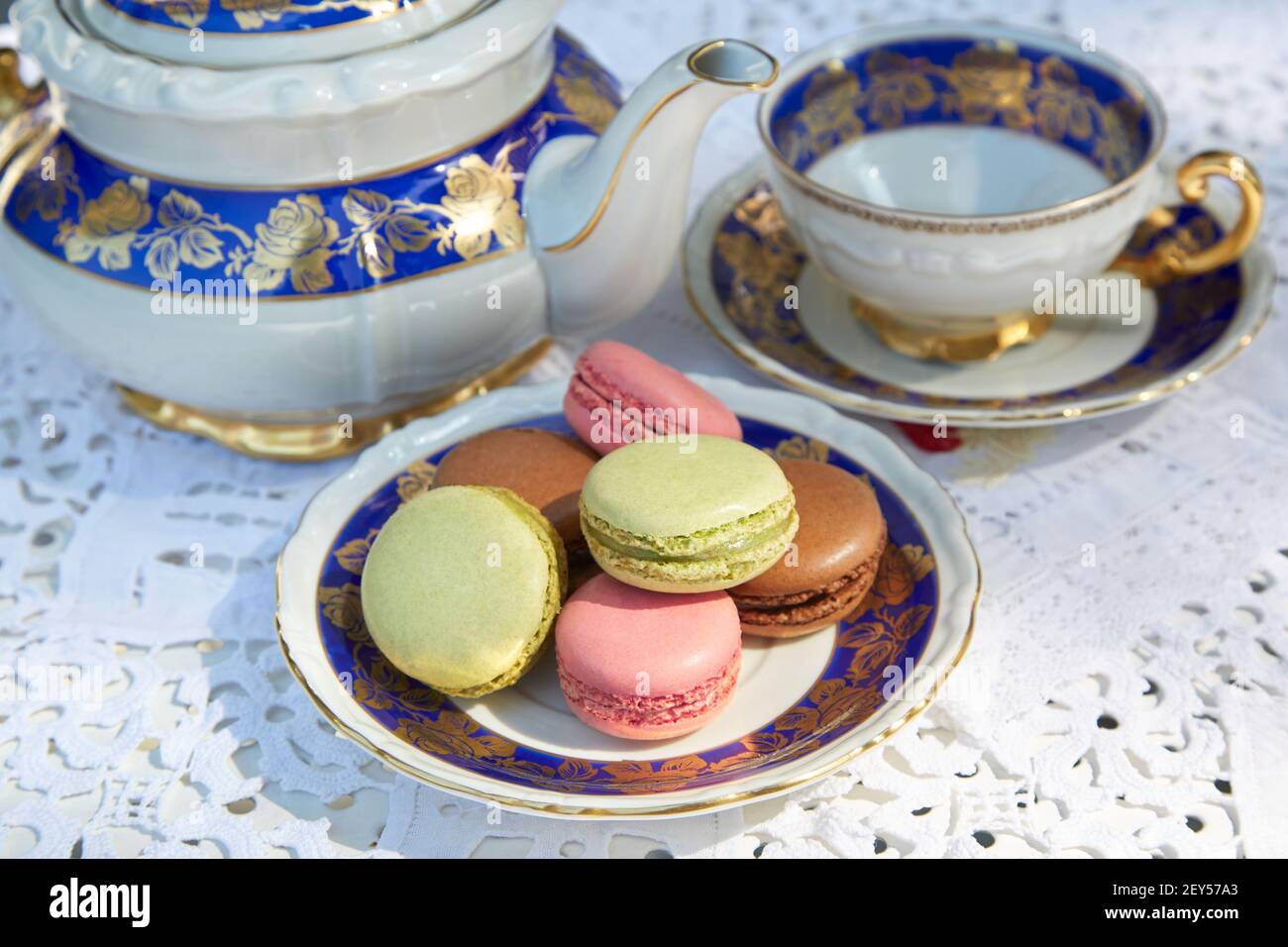 Biscotti macaron con teiera e coppa in ceramica, tovaglia ricamata bianca Foto Stock