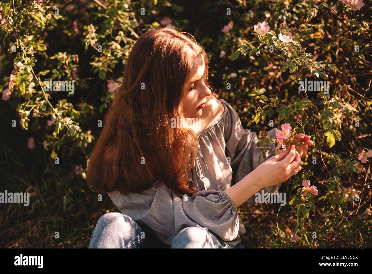 Ragazza adolescente che tiene il fiore seduto nel parco estivo durante il sole giorno Foto Stock