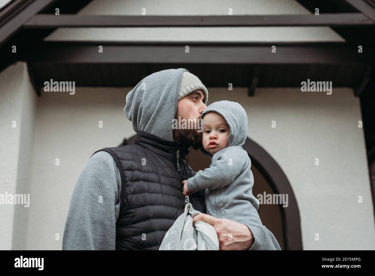 Nutrire il padre baciando il bambino in un giorno freddo con il grigio corrispondente felpe con cappuccio Foto Stock