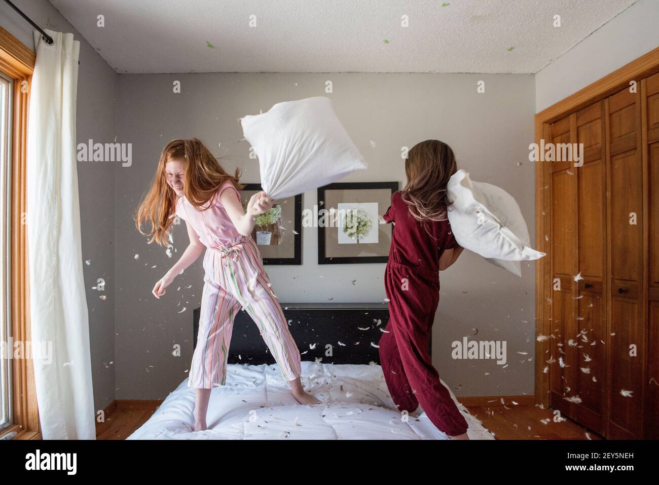 Due ragazze giovani felici che hanno una lotta cuscino di piuma sul letto. Foto Stock