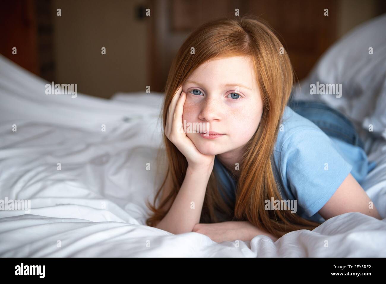 Giovane ragazza dagli occhi blu con capelli rossi felice che si posa sul letto bianco. Foto Stock