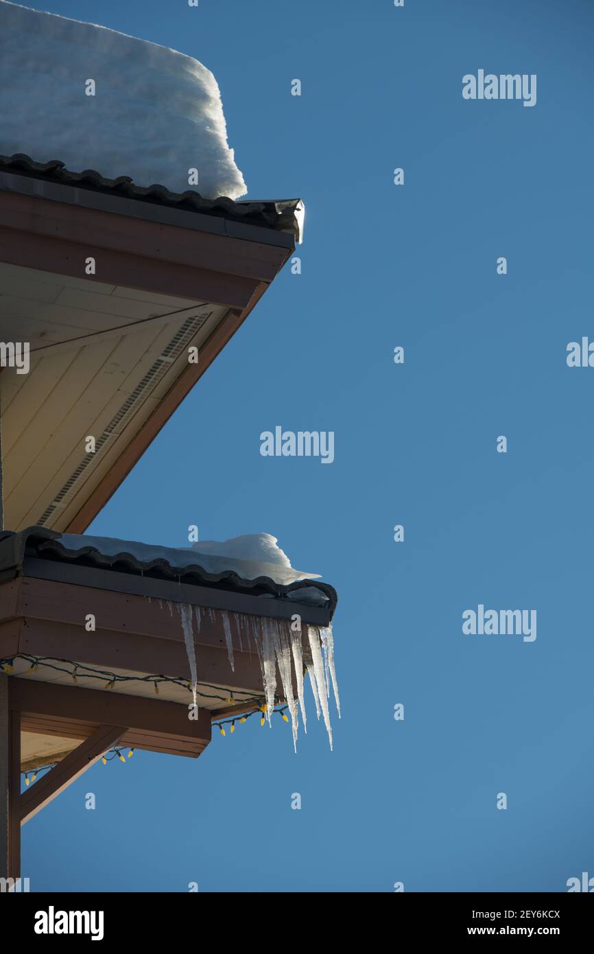 strati di neve pesanti sul tetto domestico esterno ghiacciate le ghiacciate che formano nelle grondaie attraverso le grondaie inverno casa esterno manutenzione molla effetto di congelamento di scongelamento Foto Stock