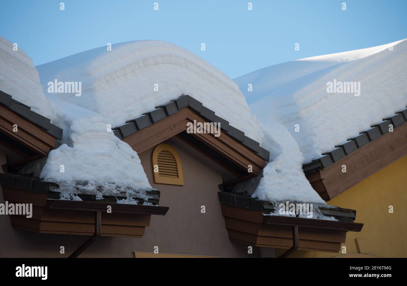 Carico di neve sul tetto di chalet da sci europeo progettato architettonicamente in inverno dopo la tempesta di neve presso la stazione sciistica neve sciolto e scongelato cielo sfondo blu Foto Stock