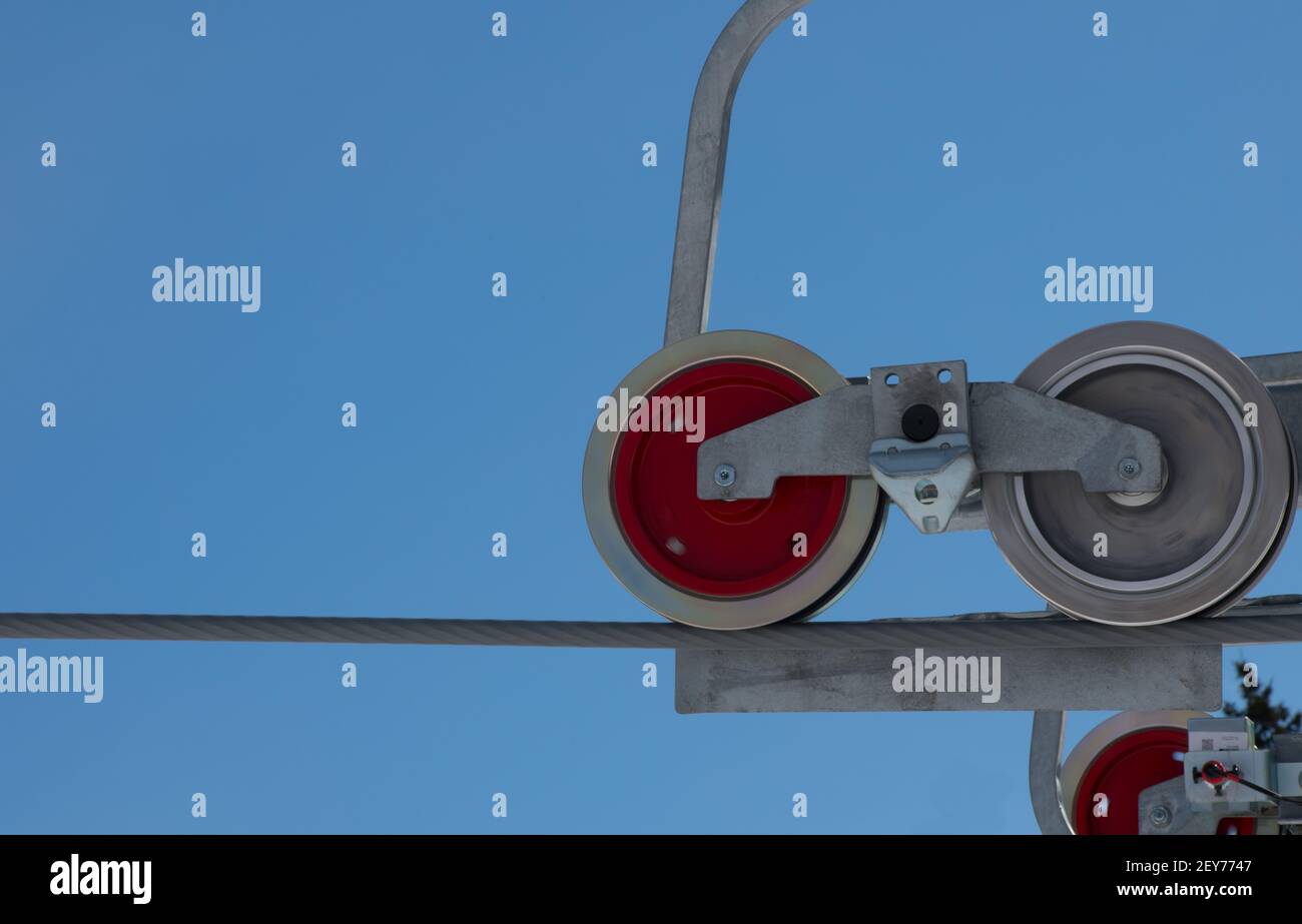 primo piano delle ruote rotonde delle pulegge di sollevamento della sedia da sci su cavo grande industriale due ruote una rossa un cielo grigio o blu argento su sfondo orizzontale Foto Stock
