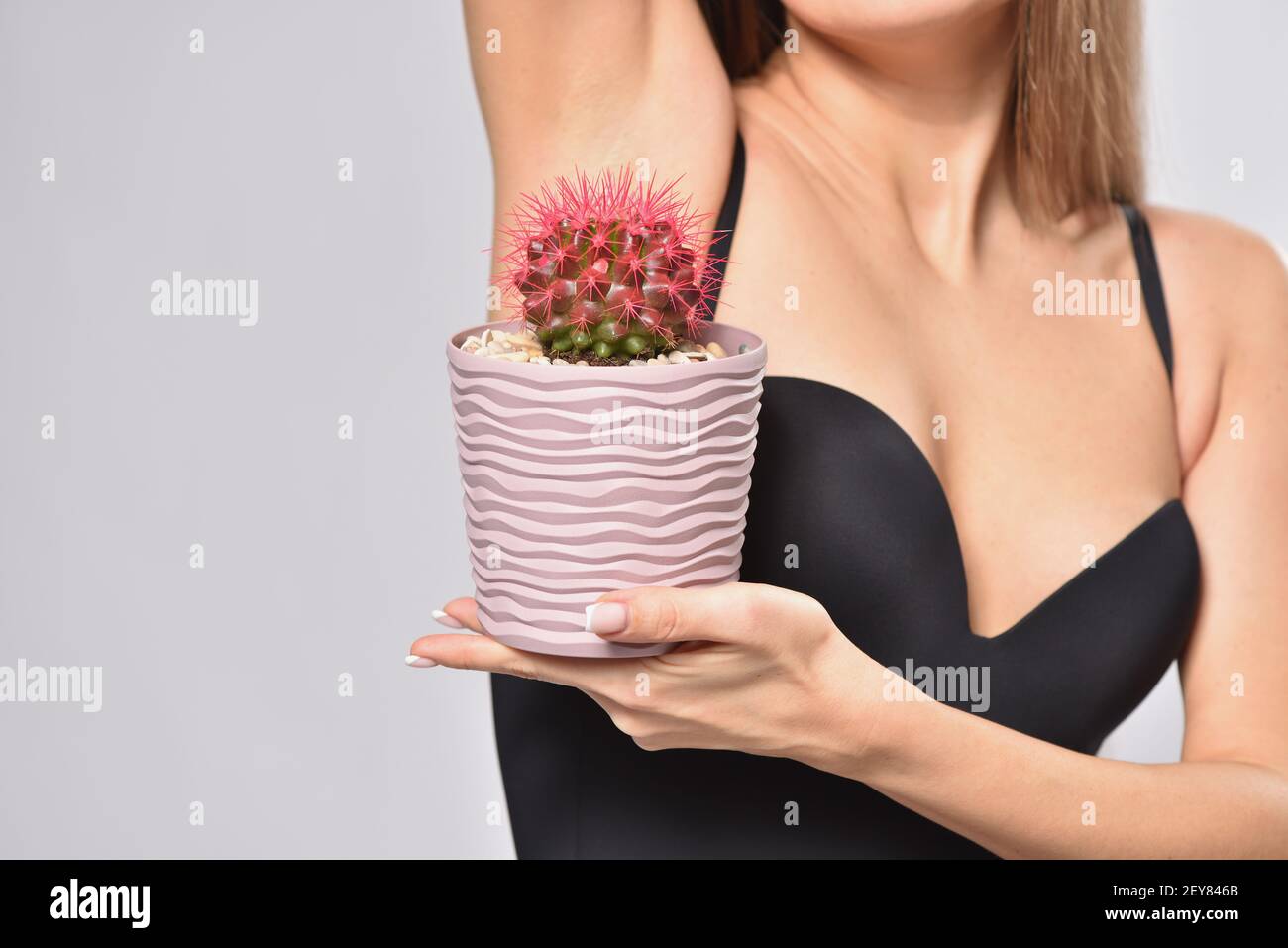 Donna che tiene cactus prickly sotto ascella, depilazione intima e concetto di igiene Foto Stock