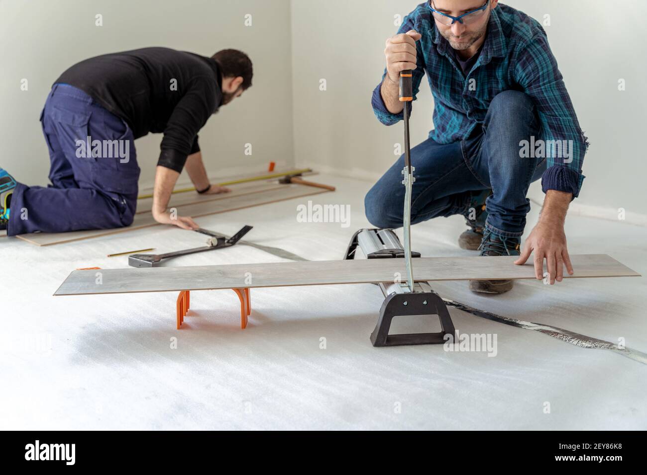 Due uomini che installano un pavimento di legno uno sta tagliando il tavole e l'altro sta installando il pavimento di legno Foto Stock
