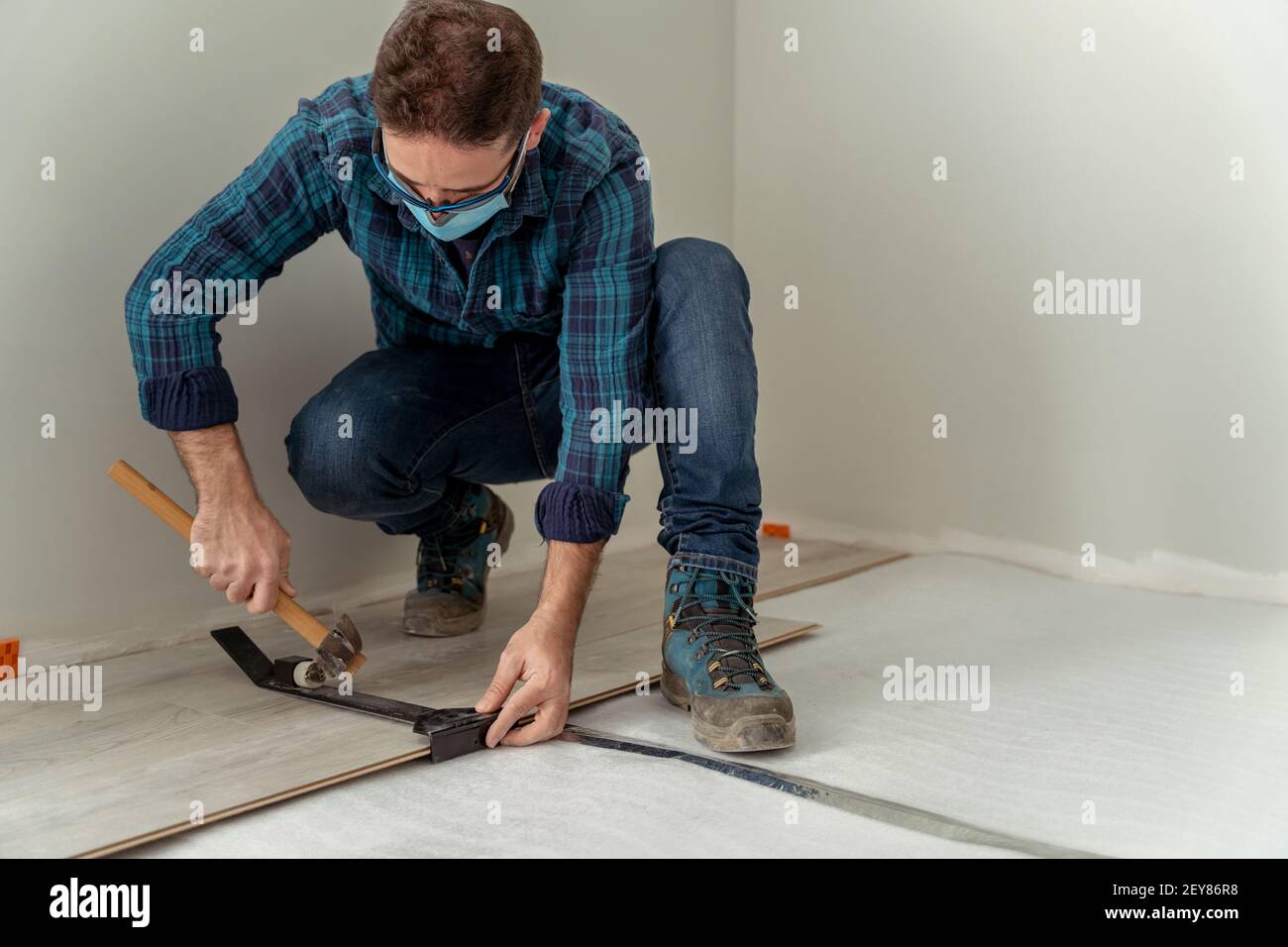 uomo con maschera installazione di un pavimento in legno con attrezzi per la sua installazione Foto Stock