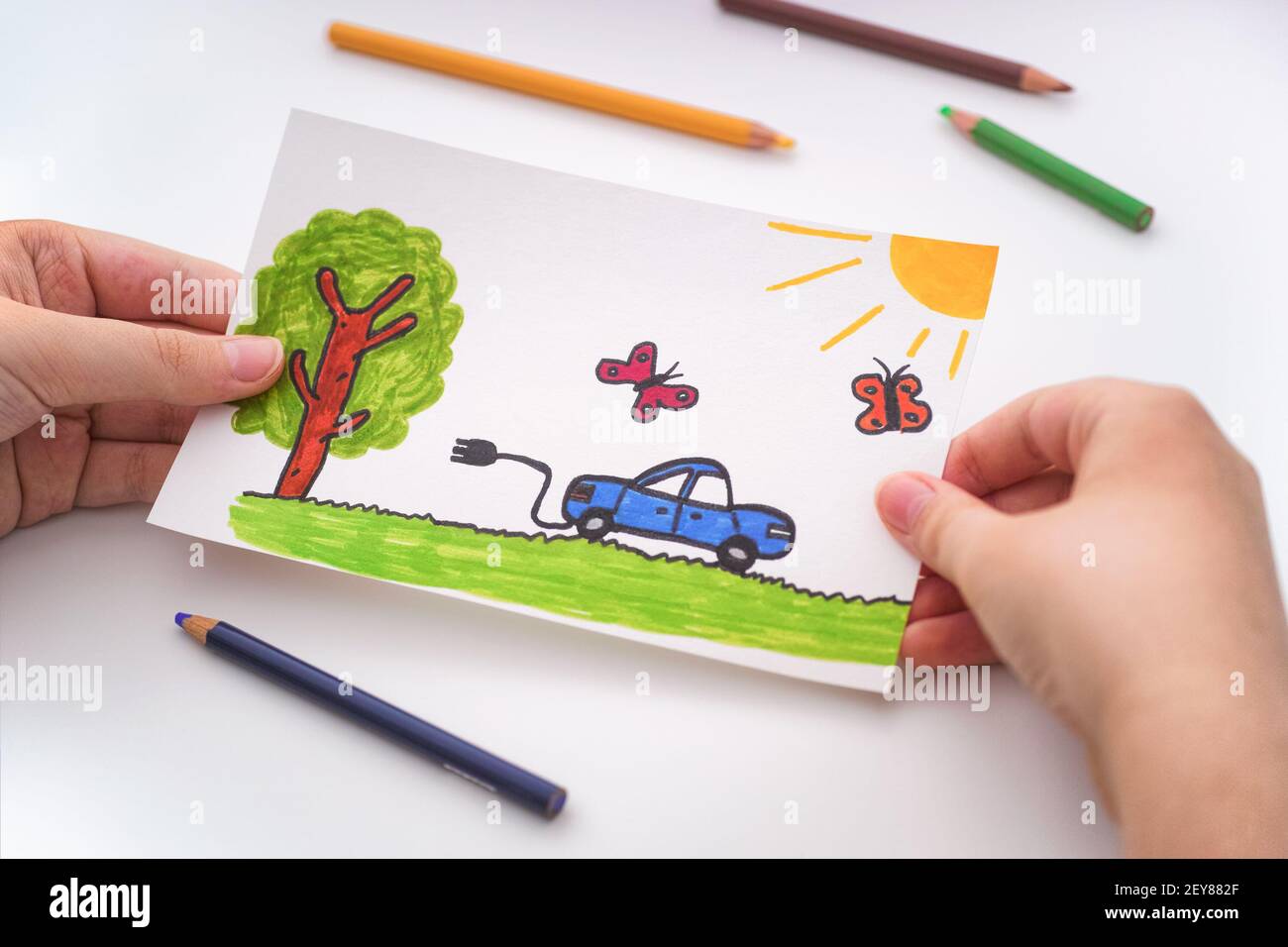 Ragazzo giovane che tiene un disegno chillike di un'automobile elettrica che va per una guida all'aperto nelle sue mani. Primo piano. Foto Stock