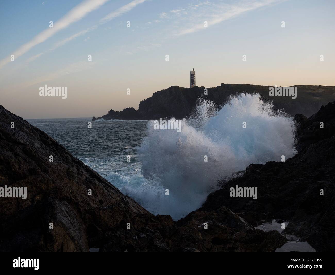 L'acqua dell'onda di mare che colpisce la rottura sulla riva rocciosa alla costa della scogliera dell'oceano atlantico Punta Frouxeira Torre del faro a Meiras Valdovino la Coruna, Foto Stock