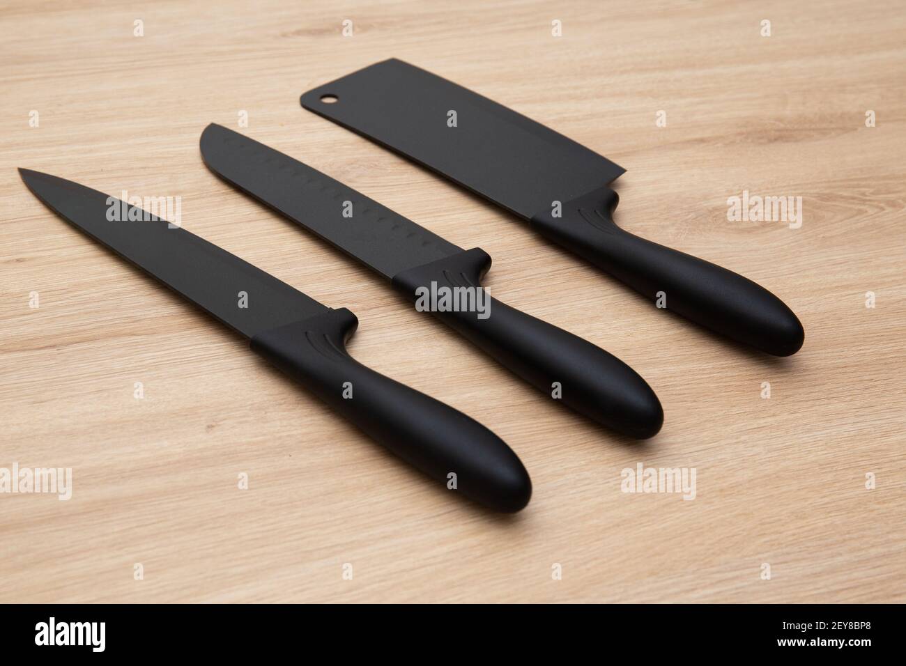 Una vista laterale di coltelli affilati neri opachi di diverse dimensioni su un tavolo di legno Foto Stock