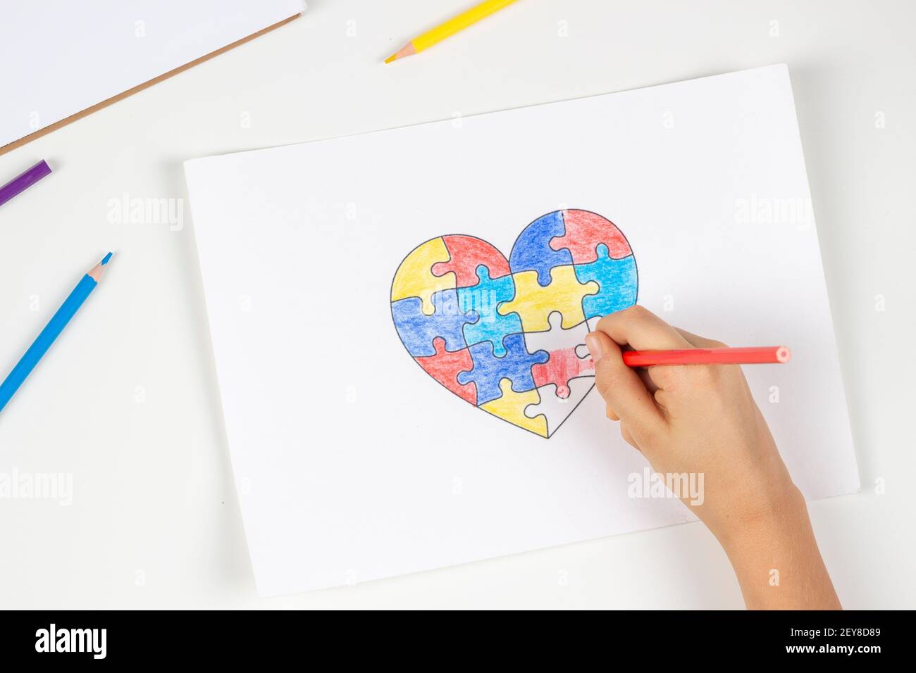Bambino mani colorazione cuore puzzle con matite colorate. Vista dall'alto. Concetto di giorno di consapevolezza autismo mondiale Foto Stock