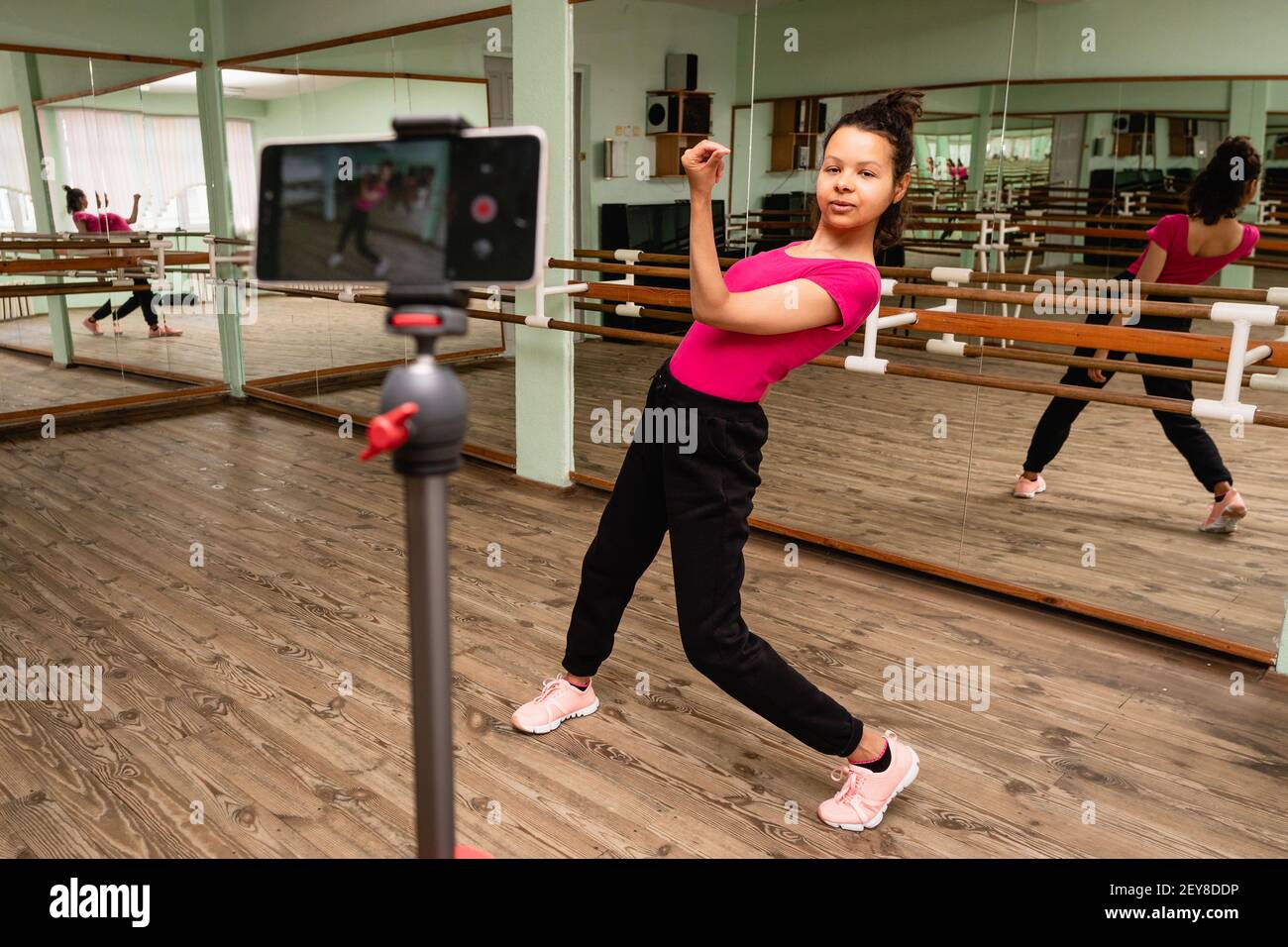 Giovane donna che registra su smartphone una lezione di danza in una sala coreografica con specchi. Lo schermo dello smartphone è fuori fuoco in primo piano. Foto Stock