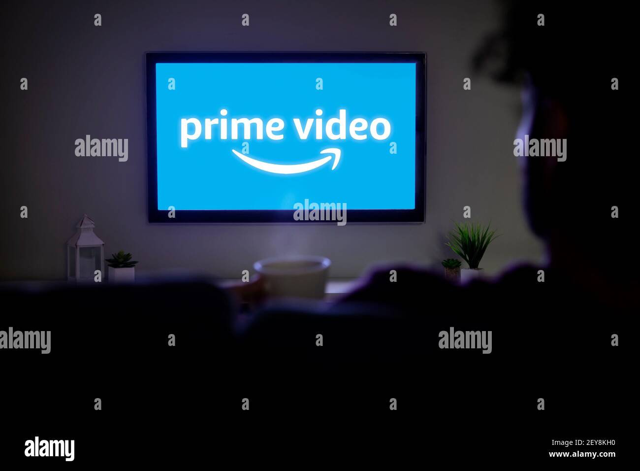 ROSARIO, ARGENTINA - 4 MARZO 2021: Logo video Amazon prime sullo schermo di LED Smart TV. Uomo afro che guarda la tv a casa con una tazza di caffè in mano. Foto Stock