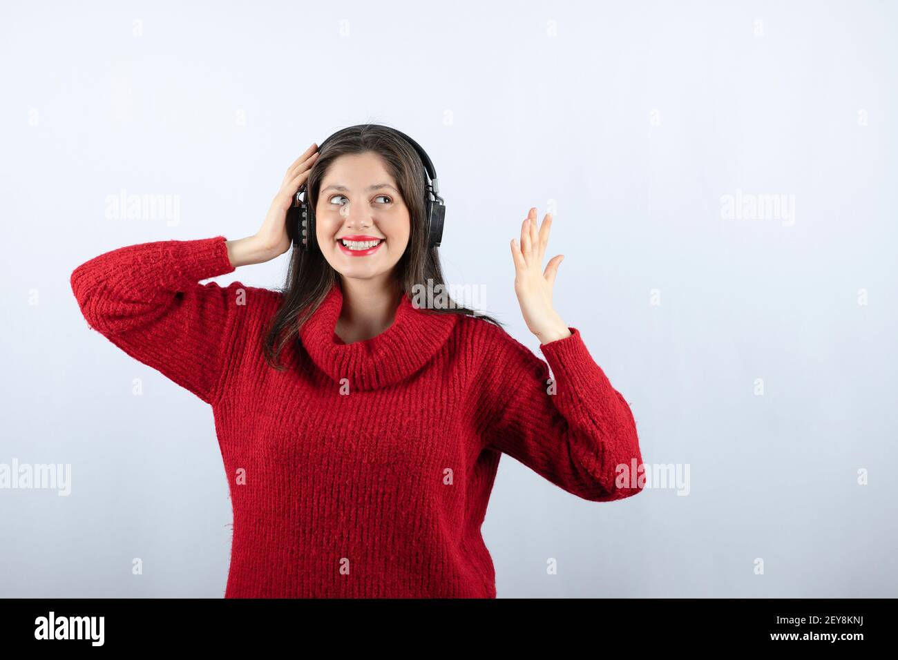 Una giovane donna sorridente in caldo pullover rosso con in piedi cuffie Foto Stock