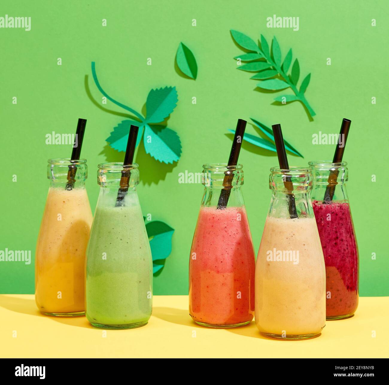 bottiglie di vari smoothies colorati di banana e di bacche su verde sfondo foglio di carta Foto Stock