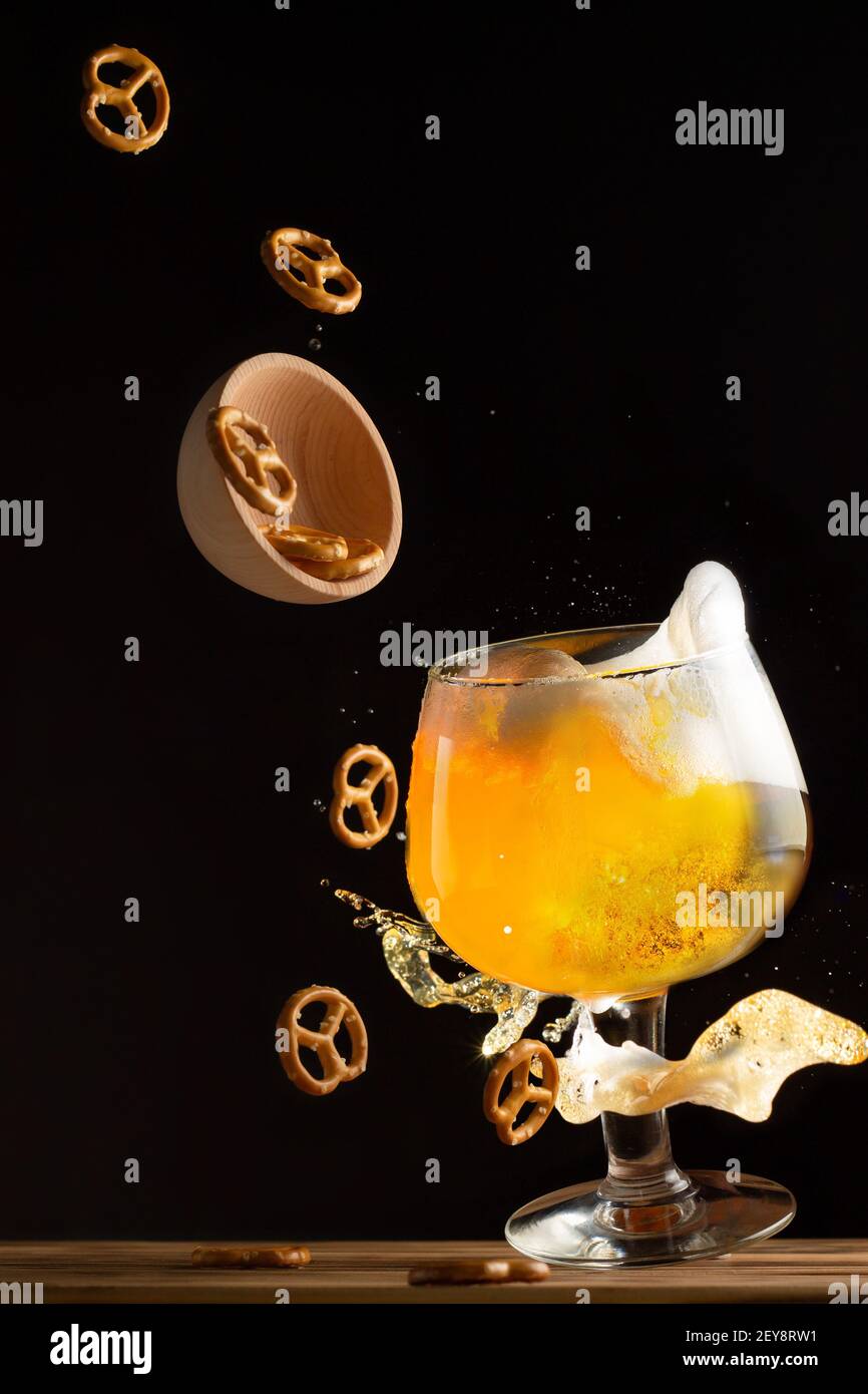 Bicchiere con spruzzi di birra e pretzel salati volanti su sfondo scuro, verticale Foto Stock